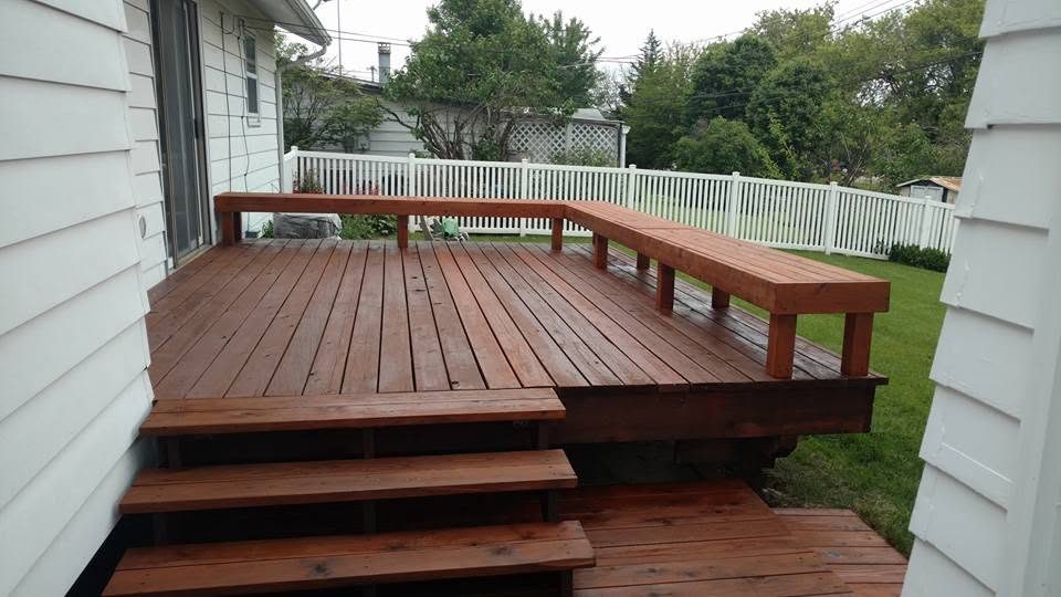 Large wooden deck with built-in benches and white railing overlooking backyard