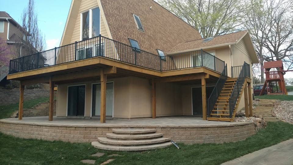 Two-story house with wooden deck, metal railings, brick foundation, and curved patio steps