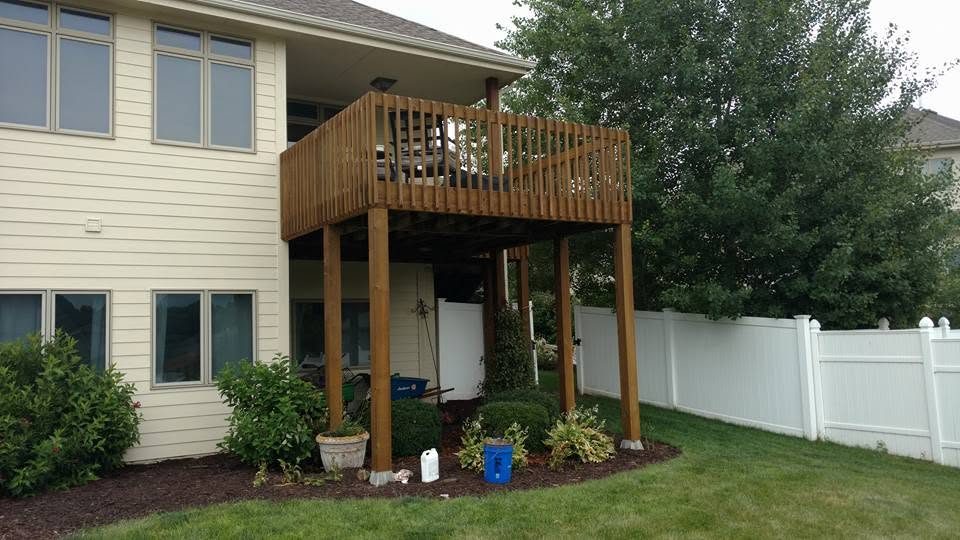 Elevated wooden deck with railing attached to cream-colored two-story house with white fence
