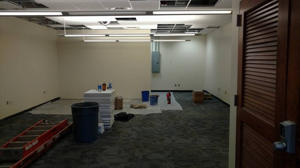 Empty commercial space under renovation with drop ceiling, carpet flooring, and construction materials