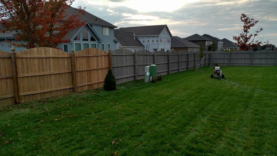 Residential backyard with wooden and gray fencing, green lawn, and houses in background