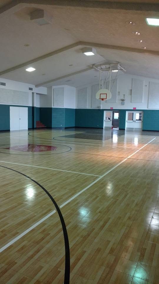 Spacious indoor gymnasium with wooden flooring, basketball hoop, and teal wall paneling