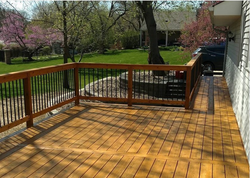 Wooden deck with black metal railings overlooking green lawn and blooming trees