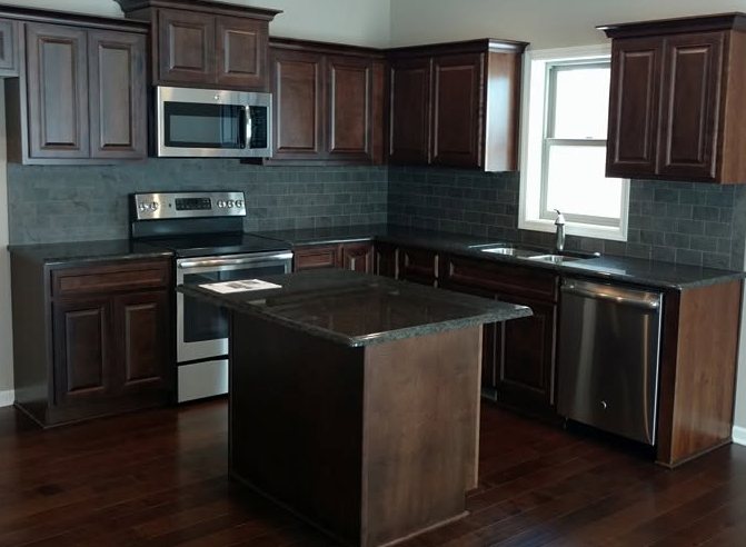Modern kitchen with dark wood cabinetry, stainless steel appliances, black island, and blue subway tile backsplash