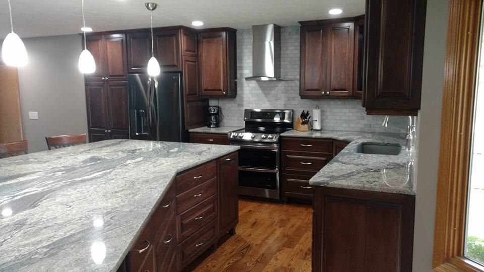Modern kitchen with dark wood cabinets, gray marble countertops, stainless steel appliances and pendant lighting