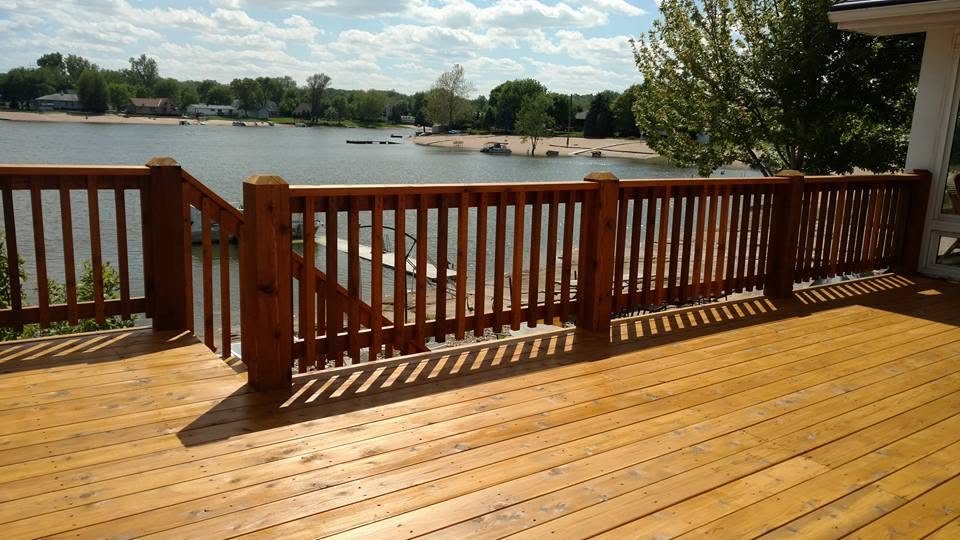 Waterfront wooden deck with brown railings overlooking a lake with boats and trees