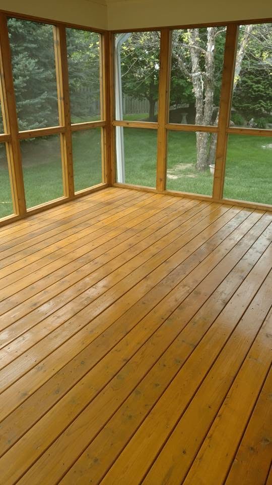 Sunlit wooden deck with large windows overlooking green lawn and trees
