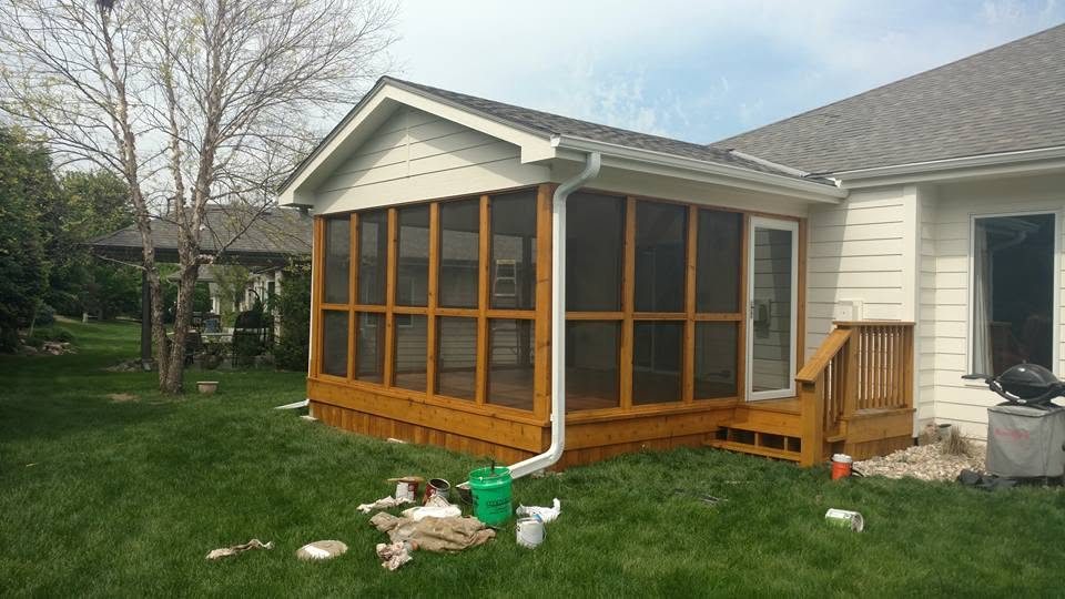 Wooden sunroom addition with large windows attached to white house with green lawn