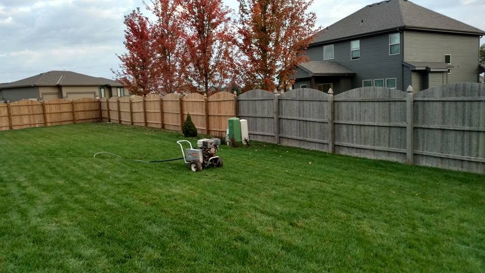 Residential backyard with green lawn, wooden fencing, and lawn care equipment near houses