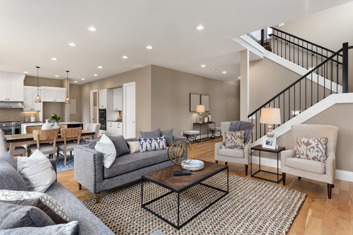 Modern open-concept living room with gray sofa, beige armchairs, wooden coffee table, and staircase