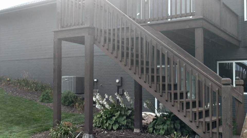 Elevated residential deck with composite railings and stairs, dark siding, landscaped foundation plantings
