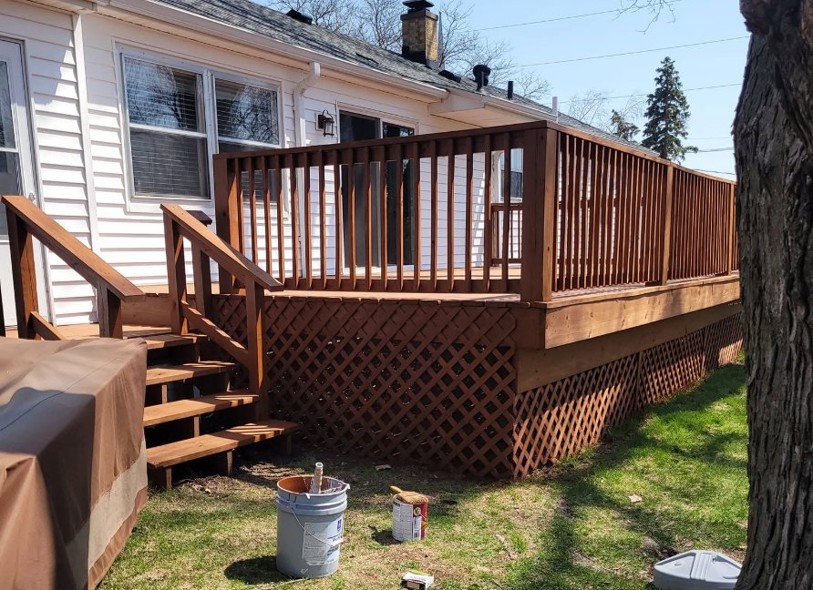 Elevated wooden deck with stairs, railings, and lattice skirting attached to white house